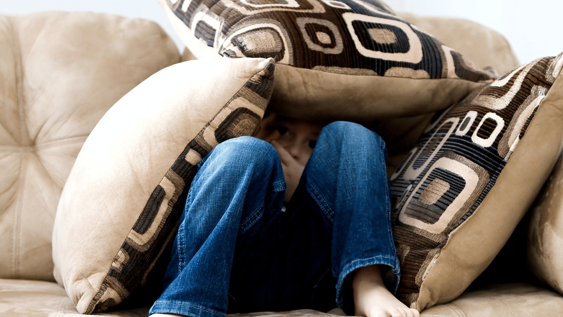 Child sat under cushions on sofa