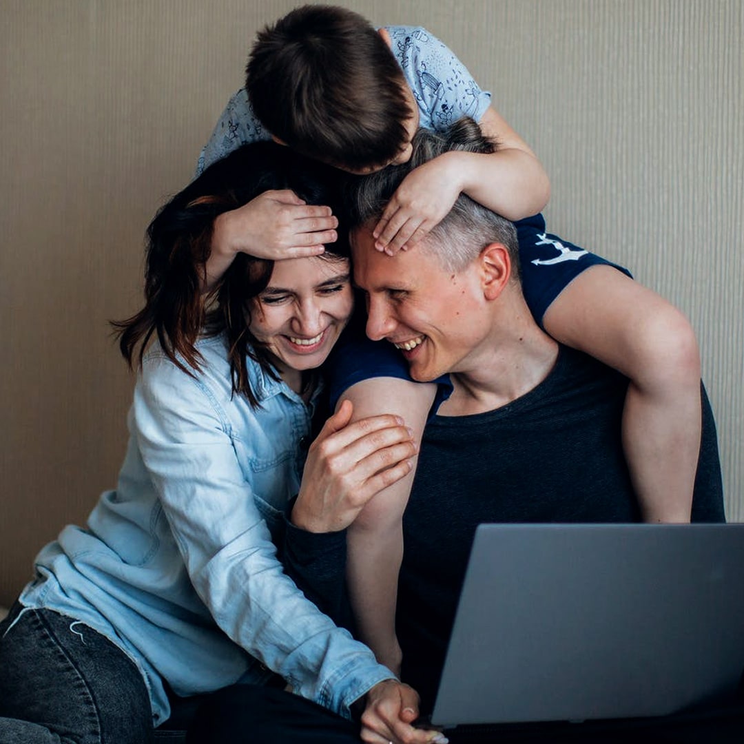 Family of three cuddling in front of laptop screen